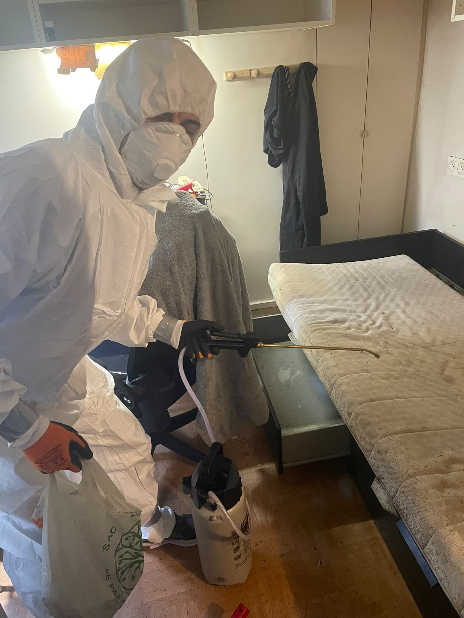 Technicien en combinaison de protection intégrale traitant un matelas infesté de punaises de lit par pulvérisation